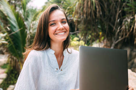Freelance concept. A freelancer girl with a laptop on her lap works out of the office while sitting on a rock near the sea. Remote work in the fresh air, modern worker. Copy spaceの写真素材