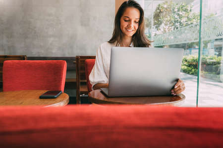 Business lady not in office. works for her laptop while sitting in a cafe. Using modern technologies in remote work. Sits at a wooden table near a large window. Reads text in a notebook. copy spaceの写真素材
