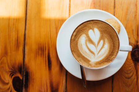 Flat lay. A cup of aromatic cappuccino with foam on a wooden table in a light cafe. Beautiful pattern on the coffee foam. Copy spaceの写真素材