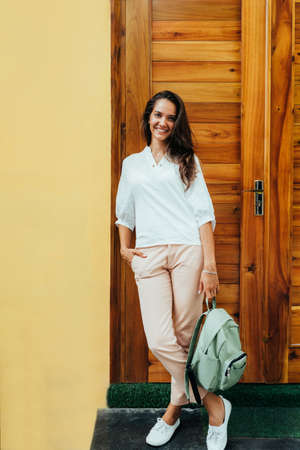 Young stylish girl in a white blouse, cream-colored trousers, white sneakers and with a green...