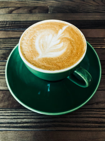Cappuccino in a green cup on brown wooden textured table flat layの写真素材
