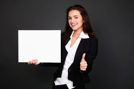 Happy smiling young business woman showing blank signboard, over grey  backgroundの写真素材