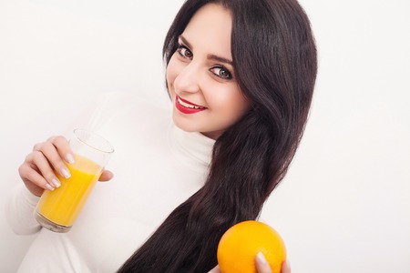 Diet. A beautiful young girl who follows the figure, drinking orange juice. The concept of healthy eating. White backgroundの写真素材