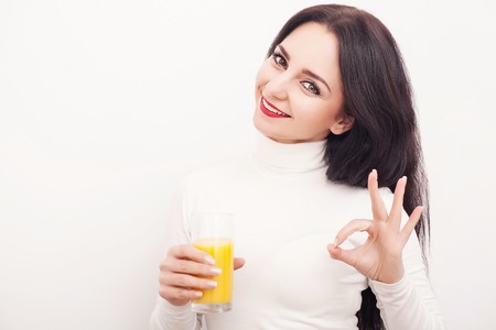 Diet. A beautiful young girl who follows the figure, drinking orange juice. The concept of healthy eating. White backgroundの写真素材