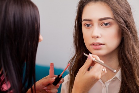 Hand of make-up master, painting lips of young beautiful model. Makeup in progress.の写真素材