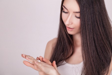 Face Treatment. Woman in Beauty Salon. Applying cosmetic cream. A beautiful young woman applying face moisturizer. Scine care of the face and hands.の写真素材