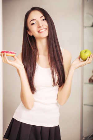 Diet. A young woman holding a pizza on the scales and make a choice between an apple and a donut. The concept of healthy eating.の写真素材