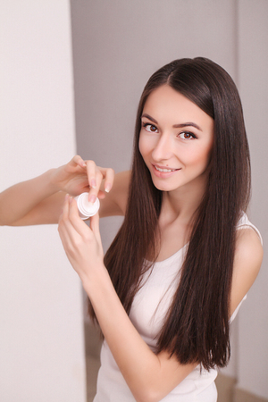 beauty, people, cosmetics, skincare and health concept - happy smiling young woman applying cream to her face.の写真素材