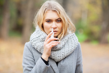 Girl sneezing in tissue. Young woman blowing her nose on the park. Woman portrait outdoor sneezing because cold and fluの写真素材