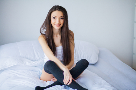 Good morning. Portrait of a smiling pretty young brunette woman relaxing in white bedの写真素材