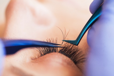 Eyelashes extensions. Fake Eyelashes. Eyelash Extension Procedure. Professional stylist lengthening female lashes. Master and a client in a beauty salonの写真素材