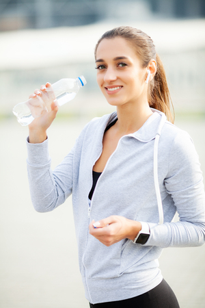 Sport outdoor. Sportive woman in headphones drinking waterの写真素材