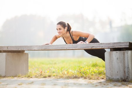 Side view of a motivated asian. Portrait of beautiful sporty woman 20s in sportswear doing push-ups, and listening to music with earbud during workout in green parkの写真素材