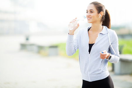 Sport outdoor. Sportive woman in headphones drinking waterの写真素材