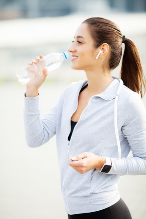 Sport outdoor. Sportive woman in headphones drinking waterの写真素材