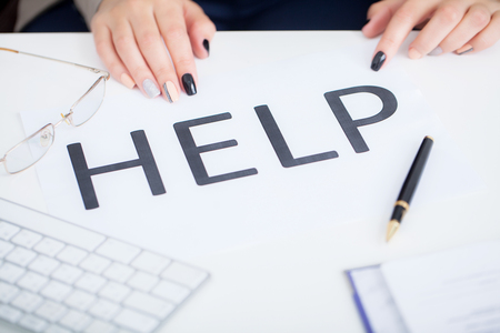 Stressed business woman imploring for help, holding a cardboard with the message Help . Focus is on the cardboardの写真素材