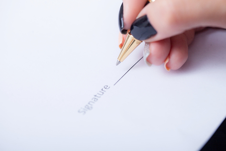 Close up girl hand putting signature on document. She situating at desk. Business concept. Low angleの写真素材