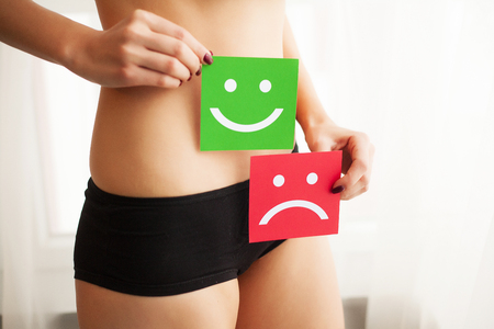 Woman Health Problem. Closeup Of Female With Fit Slim Body In Panties Holding Two Card With Sad Smiley And Happy Face Near Her Stomach. Digestive Disorders, Period Pain, Health Issues Conceptの写真素材