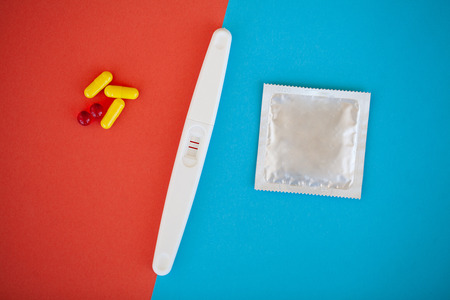 Pregnancy test. The result is positive with two strips and condom with contraceptive on colored...