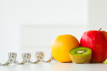 Orange, kiwi and apple surrounded by a tape measure on white backgroundの写真素材