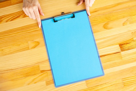 Office Hand Holding a Folder with a Blue Color Paper on the Background of the Wooden Table. Copyspace. Place for Textの写真素材