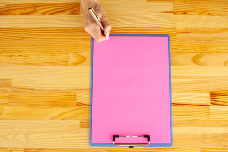 Office Hand Holding a Folder with a Pink Color Paper and Pen on the Background of the Wooden Table. Copyspace. Place for Textの写真素材