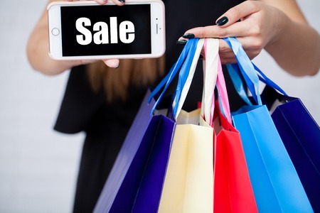 Shopping. Closeup of woman holding color paper shopping bag on white wall background