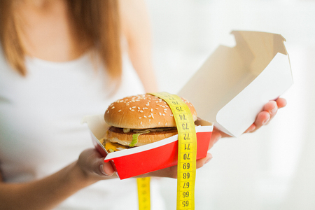 Diet. A young woman holding a burger in a measuring tape. The concept of healthy eatingの写真素材
