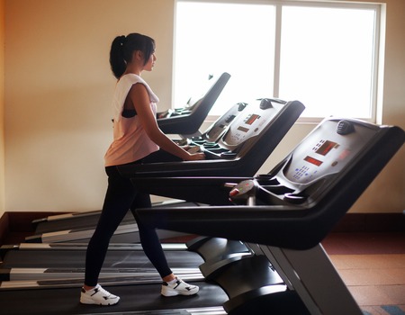 Concept of sport and healthy lifestyle. Young attractive fitness woman running on treadmill, wearing...