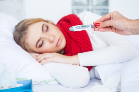 Cold And Flu. Sick woman lying on a bed with a thermometerの写真素材