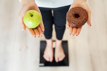 Diet. Woman Measuring Body Weight On Weighing Scale Holding Donut and apple. Sweets Are Unhealthy Junk Food. Fast Foodの写真素材