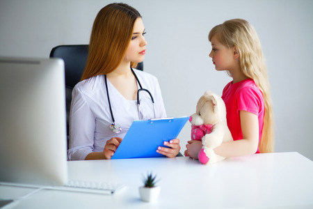 Young smiling female doctor and her little patient with teddy bear.の写真素材