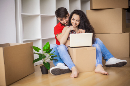 Young couple moving in new home.Sitting and relaxing after unpacking.Looking something on laptop....