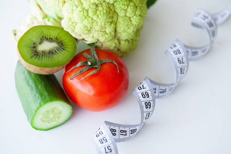 Diet. Fitness and healthy food diet concept. Balanced diet with vegetables. Fresh green vegetables, measuring tape on white background. Closeupの写真素材