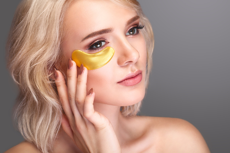 Woman Beauty Face With Mask Under Eyes. Beautiful Female With Natural Makeup And Gold Collagen Patches On Fresh Facial Skin. High Resolutionの写真素材