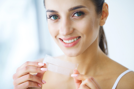 Teeth Whitening. Beautiful Smiling Woman Holding Whitening Strip. High Resolution Imageの写真素材