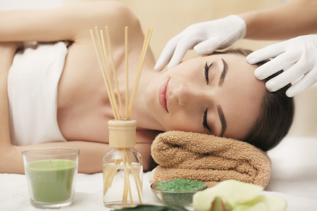 Beautiful young woman getting facial massage lying on the couch. Top view focused on the faceの写真素材