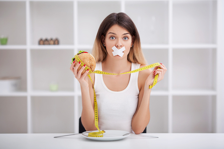 Diet. The concept of healthy and unhealthy nutrition. The model plus size makes a choice in favor of healthy food and fruit by refusing fast food and burger. XXL womanの写真素材