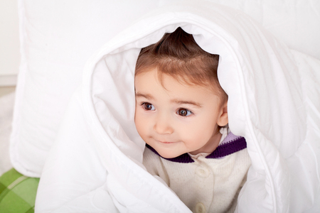 Portrait of baby girl lying in bed under featherbedの写真素材