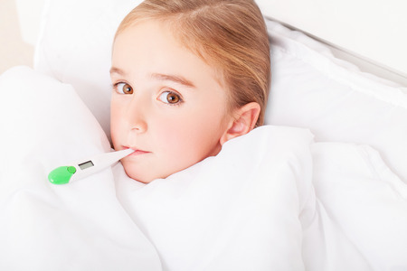 Flu. Young girl lying in bed with a thermometerの写真素材