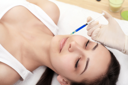 Woman receiving a injection in the lips zone lying in bathrobe on the medical couchの写真素材