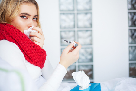 Sick Woman. Woman with flu virus lying in bed, she is measuring her temperature with a thermometerの写真素材