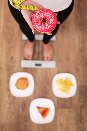 Young beautiful woman standing on scales and holding a donut. The concept of healthy eating. Healthy Lifestyle. Diet.の写真素材