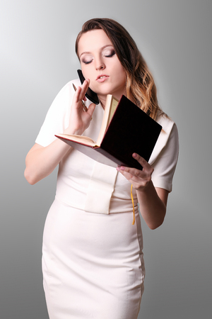 Beautiful female clerk standing in office at her workplace, holding planner, reading timetable for the day, side view portraitの写真素材
