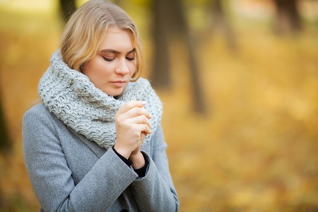 Cold and flu. Young woman in a gray coat walking in the autumn park and warms frozen handの写真素材