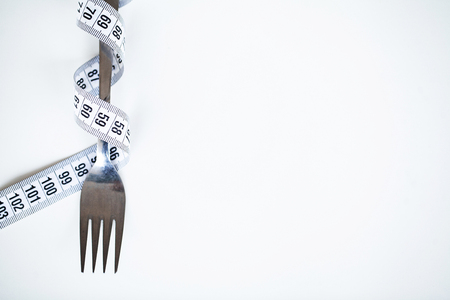 Diet or weight control concept. Centimeter tape and fork on a white background with a place for inserting text. concept of health, weight loss, diet, proper nutritionの写真素材