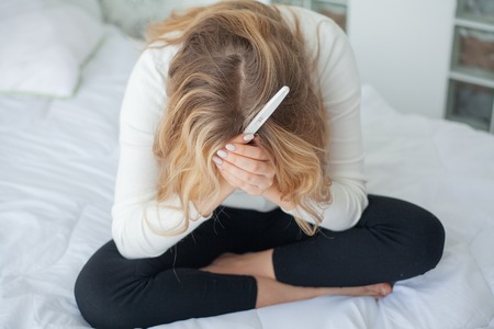 Girl looking at pregnancy test. Sad woman waiting pregnant test resultsの写真素材