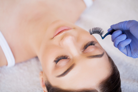 Eyelashes extensions. Fake Eyelashes. Eyelash Extension Procedure. Professional stylist lengthening female lashes. Master and a client in a beauty salonの写真素材