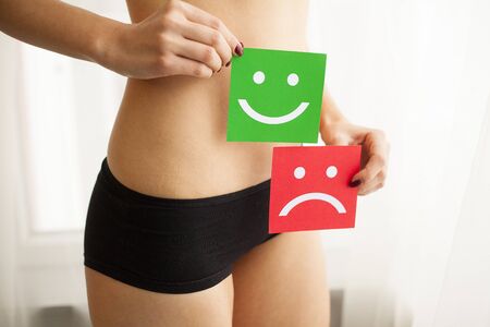 Woman Health Problem. Closeup Of Female With Fit Slim Body In Panties Holding Two Card With Sad Smiley And Happy Face Near Her Stomach. Digestive Disorders, Period Pain, Health Issues Conceptの写真素材