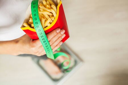 Diet. Woman standing on scales and holding a potato chips. The concept of healthy eating. Healthy...